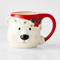 a ceramic mug with a bear's head and holly decorations on it, sitting on a white surface