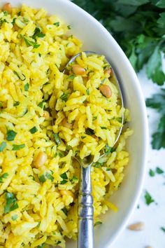 a white bowl filled with yellow rice and garnished with parsley next to a spoon