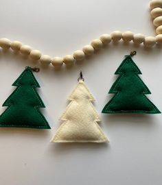 three felt christmas trees are hanging on a beaded necklace