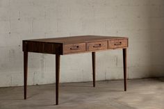 a wooden desk with two drawers in front of a white brick wall and concrete floor