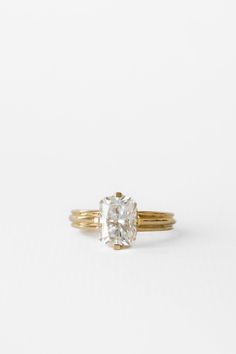 an oval cut diamond sits on top of a gold band, set against a white background