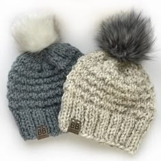 two knitted hats with grey and white pom - poms, one is blue