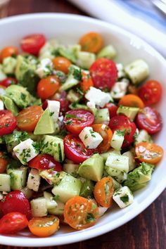 a white bowl filled with cucumber, tomato and avocado salad on top of a wooden table