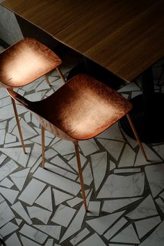 two wooden chairs sitting on top of a white tiled floor next to a brown table