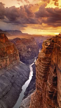 the sun is setting at the edge of a canyon with water below it and clouds in the sky