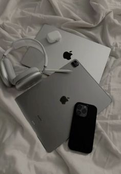 an apple laptop, headphones and iphone on a white sheet with a pair of earbuds