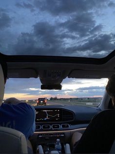 two people in a car driving down the road at dusk with dark clouds behind them