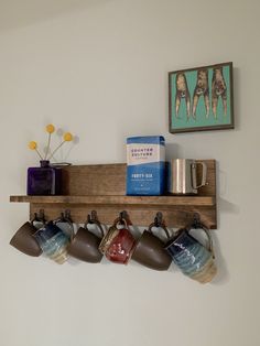 coffee mugs are lined up on a wooden shelf with cups hanging from the hooks