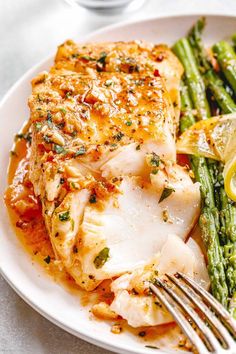 a white plate topped with chicken, asparagus and lemon wedges next to a fork