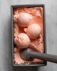 three scoops of pink ice cream in a metal container with a spoon next to it