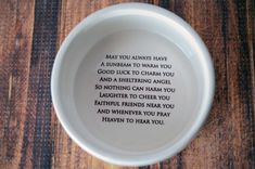 a white bowl with a poem written in it on top of a wooden table next to a wall