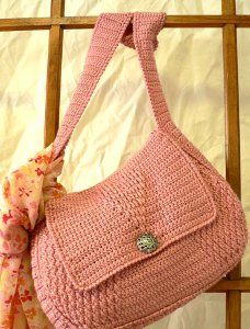 a pink crocheted purse with a bow on the front and shoulder hanging from it