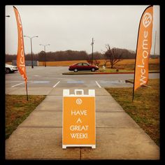 an orange sign sitting on the side of a road next to a parking lot filled with cars