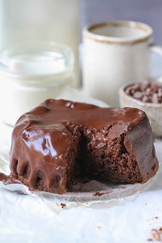 a chocolate cake on a plate with one piece missing from it and two cups of milk in the background