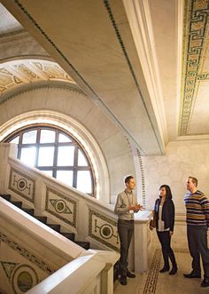 two men and a woman are standing on the stairs in an ornately decorated building