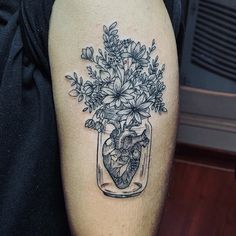 a person with a tattoo on their arm holding a vase filled with flowers and a heart