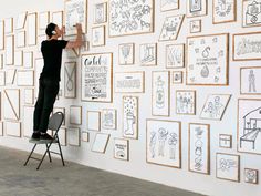 a man standing on a chair in front of a wall covered with drawings