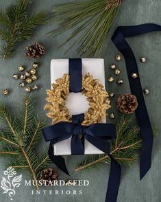 a gift wrapped in white paper with a blue ribbon and pine cones on the side