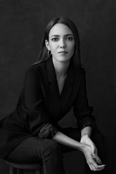 a black and white photo of a woman sitting on a stool with her hands in her pockets