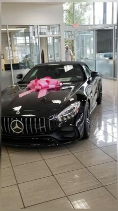 a black car with a pink bow on it's hood in a showroom