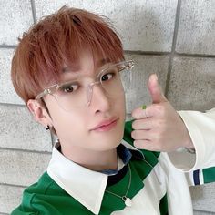 a young man wearing glasses giving the thumbs up sign in front of a brick wall