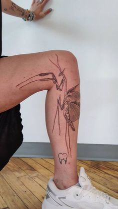 a person with a tattoo on their leg sitting down in front of a white wall