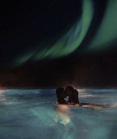 two people are kissing in the water under an aurora bore