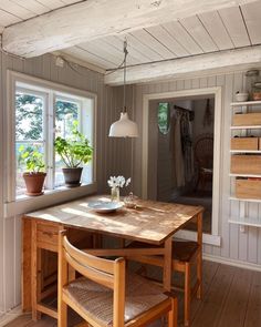 a wooden table sitting under a window next to a potted plant on top of a hard wood floor