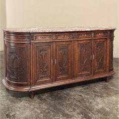 an ornately carved wooden sideboard with marble top and doors on the front, in a room