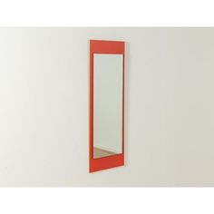 a mirror mounted to the side of a white wall next to a red cabinet and shelf