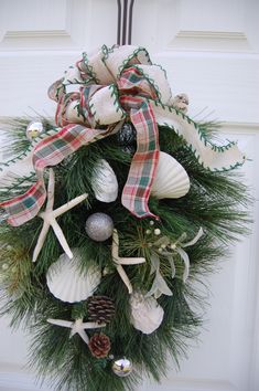 a wreath with seashells and pine cones hanging on a door