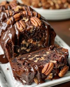 chocolate cake with pecans on top sitting on a white plate next to another piece of cake