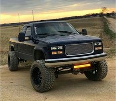 a black truck parked on top of a dirt road next to a dry grass field