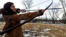 a man with long hair holding a bow and arrow in his hand while standing in the snow