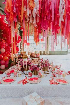 a table set up for a party with pink, orange and red decorations hanging from the ceiling