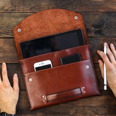 a person holding a cell phone in their leather pouch with pen and paper on the table