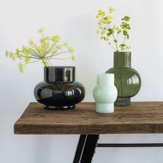 three vases are sitting on a table with flowers in the middle and one is green