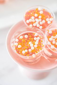 three glasses filled with candy and sprinkles on top of a pink plate