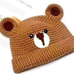 a brown teddy bear knitted hat sitting on top of a white table next to a piece of paper