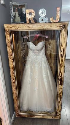 a wedding dress is displayed in a wooden frame