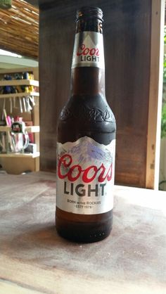 a bottle of booze light sitting on top of a wooden table next to a window