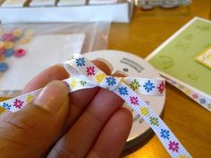 a person is holding a white ribbon with colorful flowers on it and some other items in the background