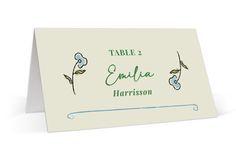 a place card with blue flowers on the front and green leaves on the back, which reads table 2 entia harrison