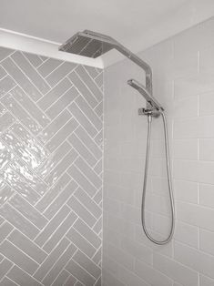 a shower head and hand held shower faucet in a white bathroom with herringbone tile