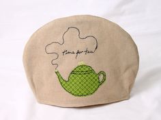 a tea pot cover with a green teapot embroidered on the front, and words time for tea written in cursive writing