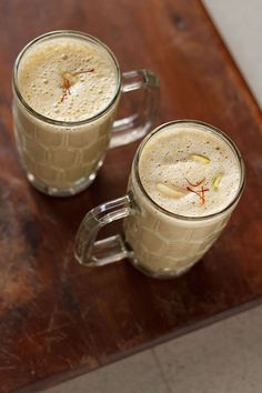 two mugs of coffee sitting on top of a wooden table next to each other