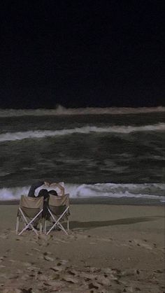 a man sitting in a chair on the beach at night with his back turned to the camera