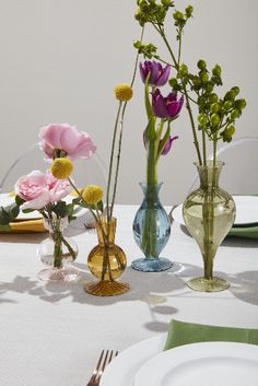 there are three vases with flowers in them on the dining room table set for dinner