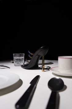 a white table topped with plates and silverware next to a black high heeled shoe