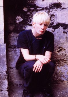 a young man sitting on the ground next to a wall